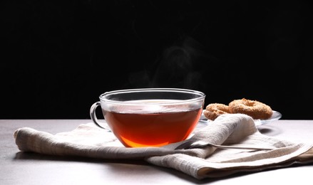 Glass cup of tea with cookies on table against black background