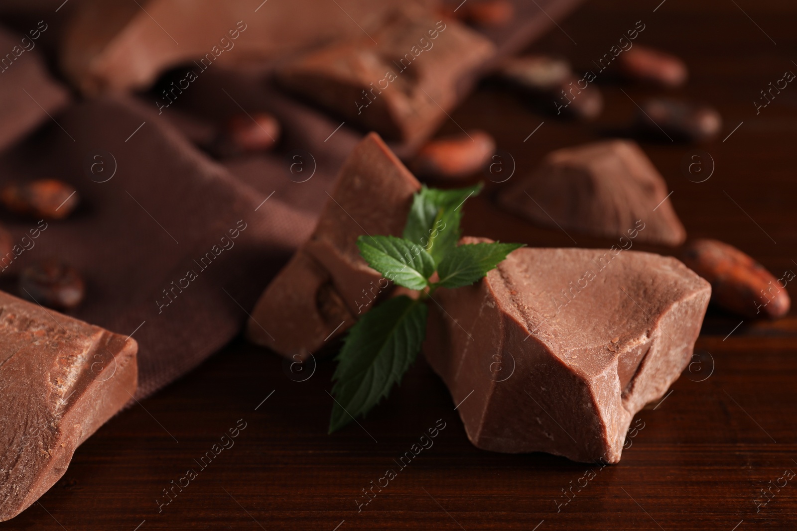 Photo of Pieces of tasty milk chocolate and mint on wooden table, closeup