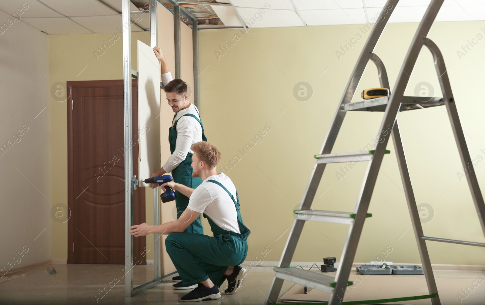 Photo of Young workers installing drywall indoors. Home repair service