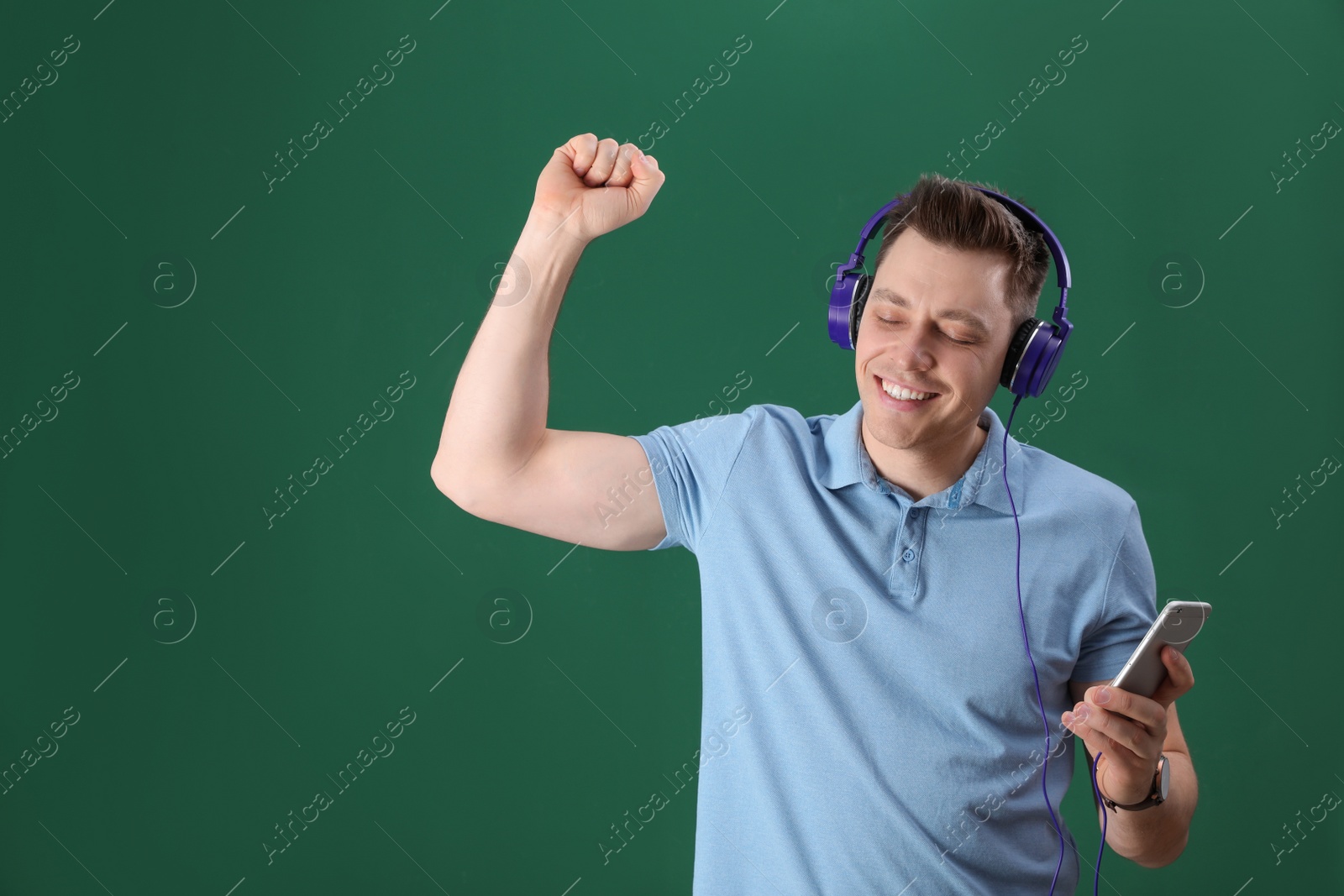 Photo of Man in headphones with mobile device on color background. Space for text