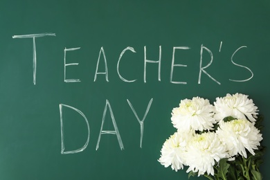 Words TEACHER'S DAY and chrysanthemum flowers on green chalkboard, top view