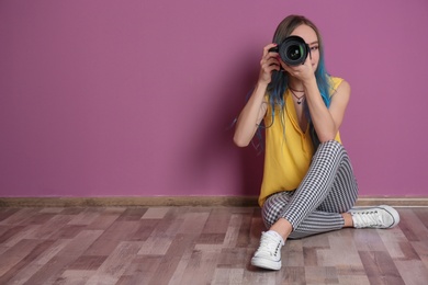 Young female photographer with camera near color wall