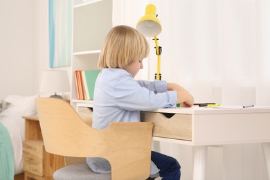 Cute little boy playing with colorful wooden cubes at desk in room. Home workplace
