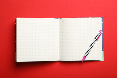 Stylish open notebook and pen on red background, top view