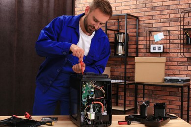 Repairman with screwdriver fixing coffee machine at table indoors