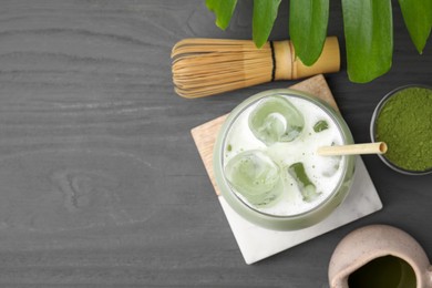 Photo of Glass of tasty iced matcha latte, bamboo whisk, leaf and powder on grey wooden table, flat lay. Space for text