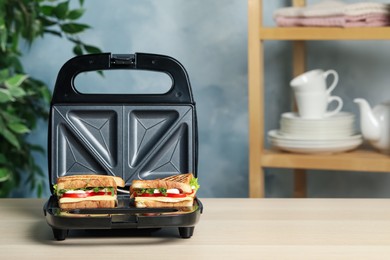 Modern grill maker with sandwiches on light wooden table, space for text