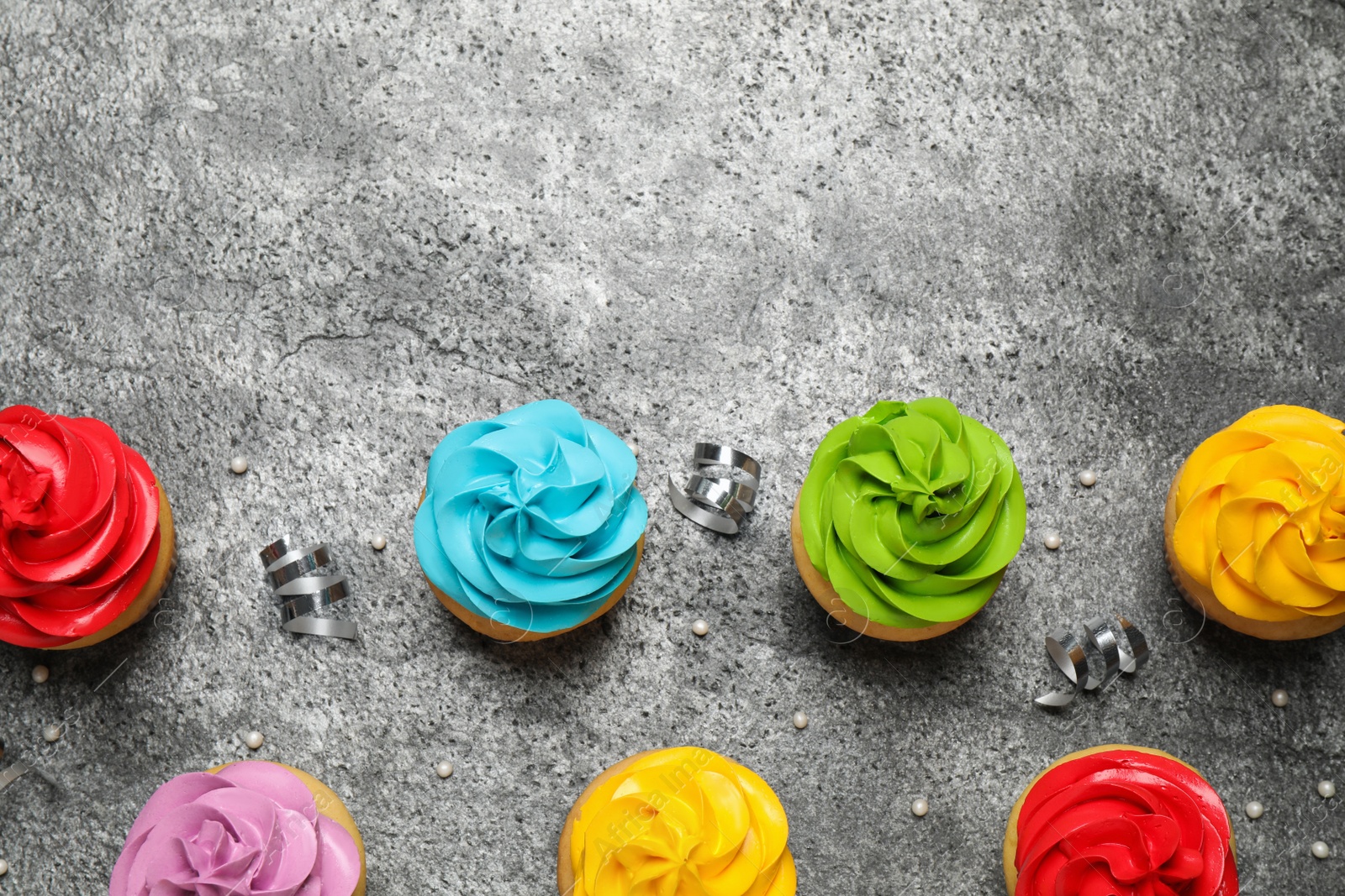 Photo of Flat lay composition with colorful birthday cupcakes on grey table. Space for text