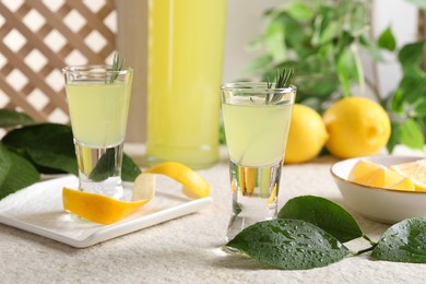 Photo of Tasty limoncello liqueur and green leaves on light textured table