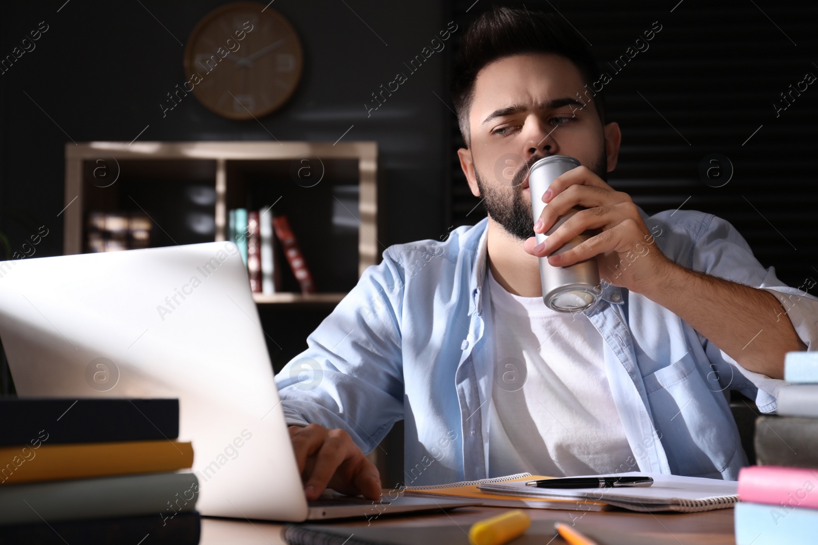 Photo of Tired young man with energy drink studying at home