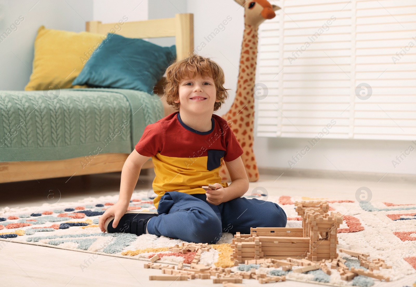 Photo of Little boy playing with wooden construction set on carpet in room. Child's toy