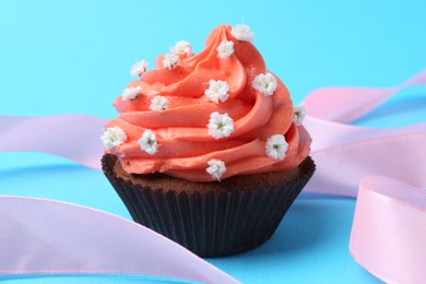 Delicious cupcake with bright cream and flowers on light blue background