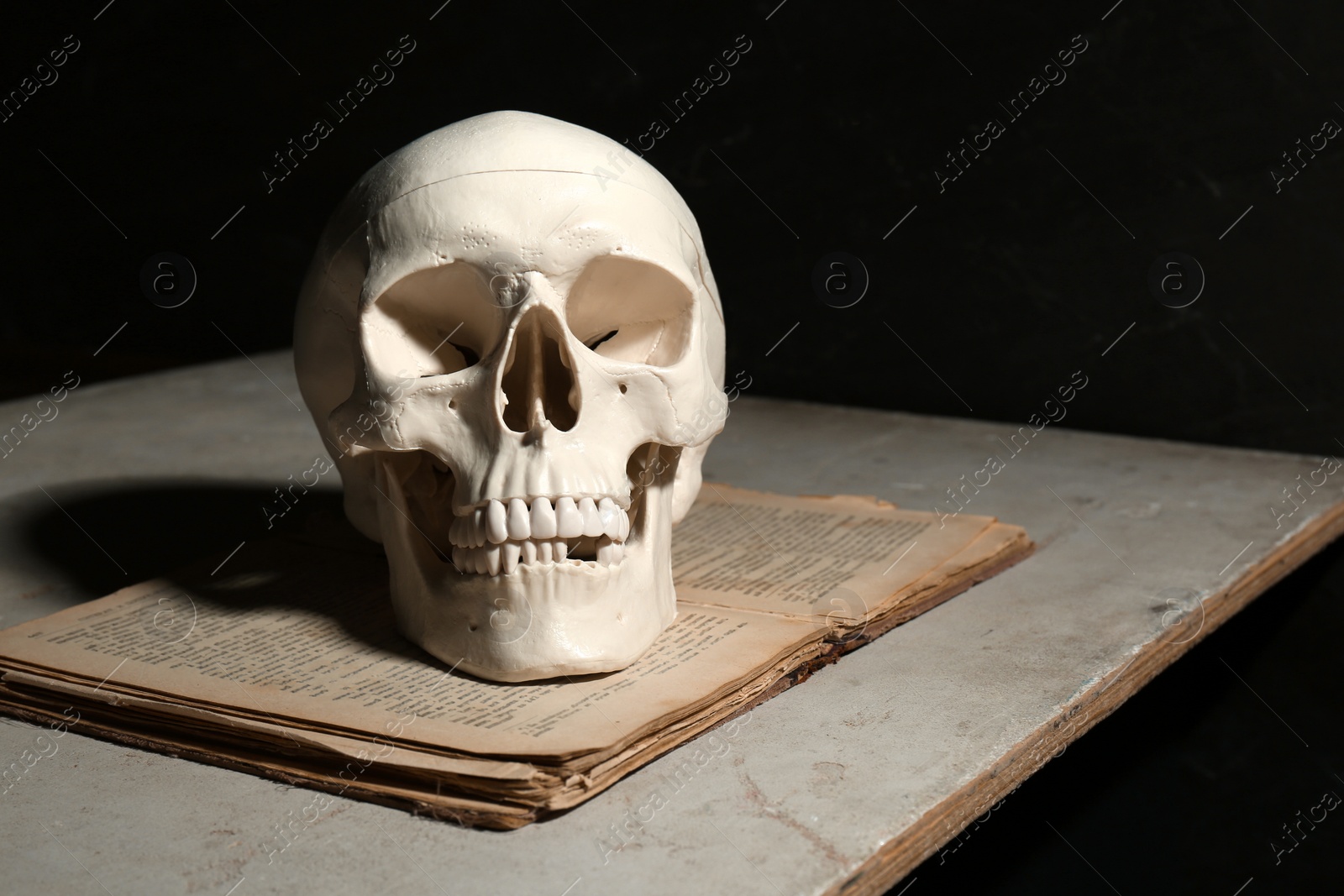 Photo of Human skull and old book on table against black background, space for text