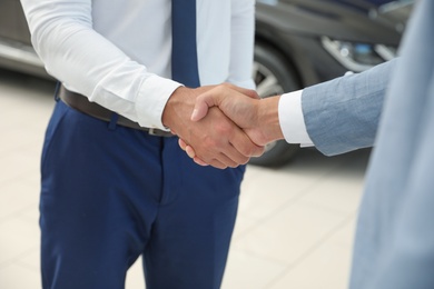 Young salesman shaking hands with client in modern car dealership, closeup