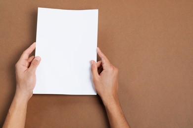 Photo of Man holding sheet of paper on brown background, closeup. Mockup for design
