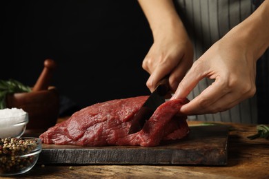 Woman cutting fresh raw meat at wooden table, closeup