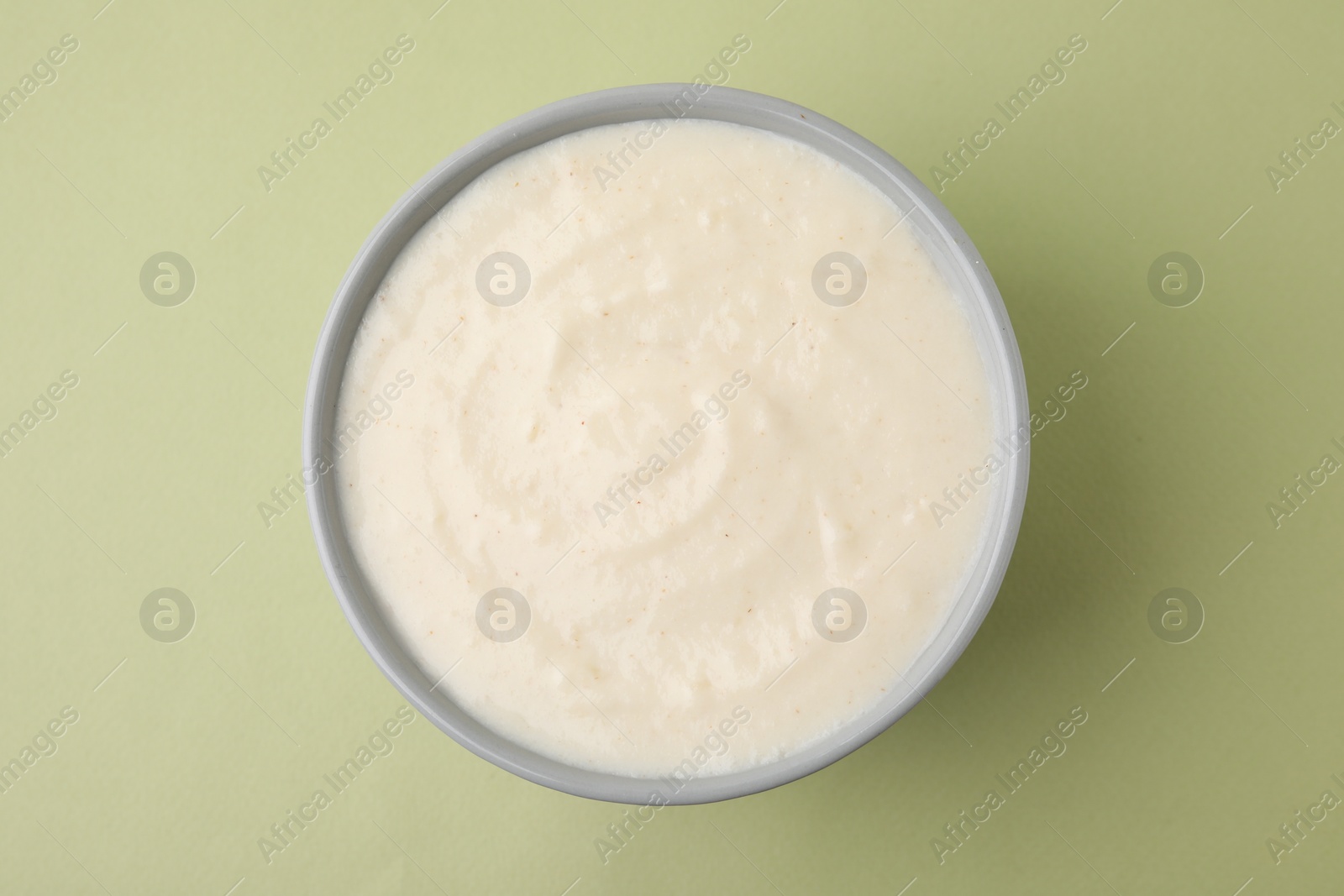 Photo of Delicious semolina pudding in bowl on light olive table, top view