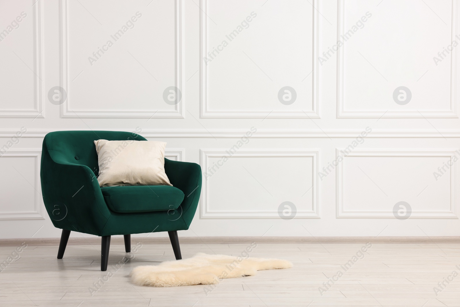 Photo of Comfortable armchair with cushion near white wall indoors. Space for text