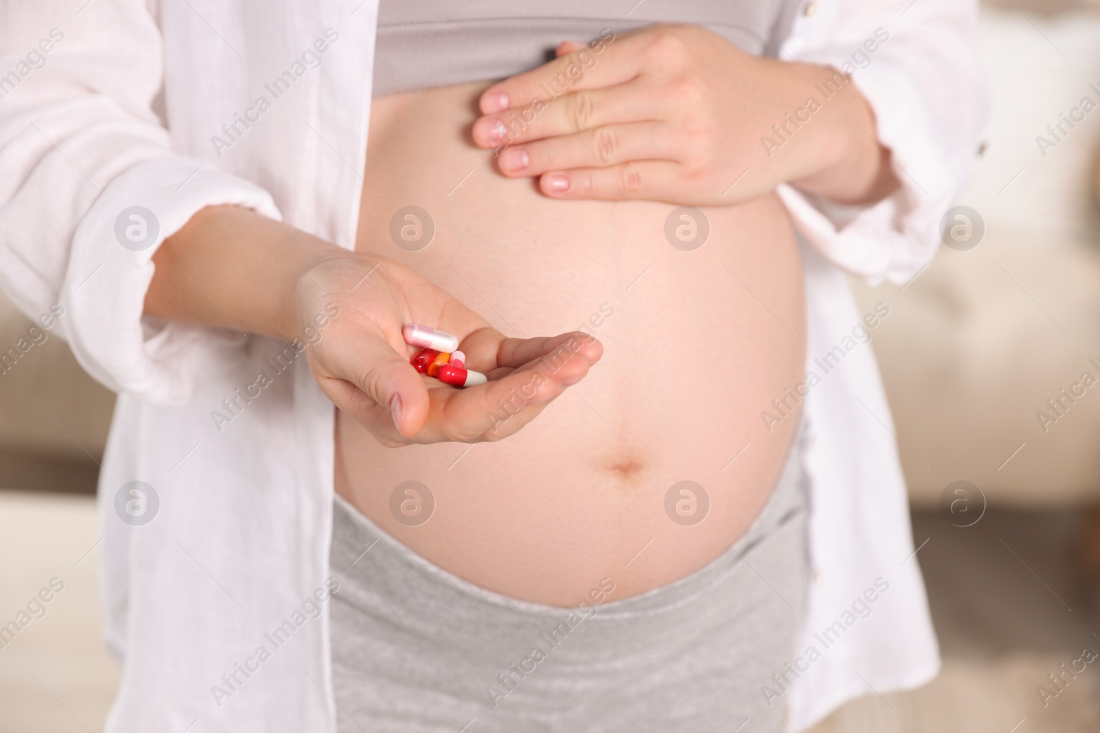Photo of Pregnant woman holding pile of pills at home, closeup