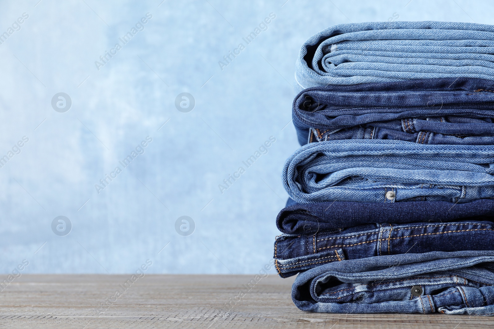 Photo of Stack of different jeans on wooden table against blue background. Space for text