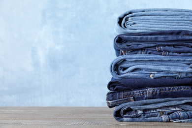 Photo of Stack of different jeans on wooden table against blue background. Space for text