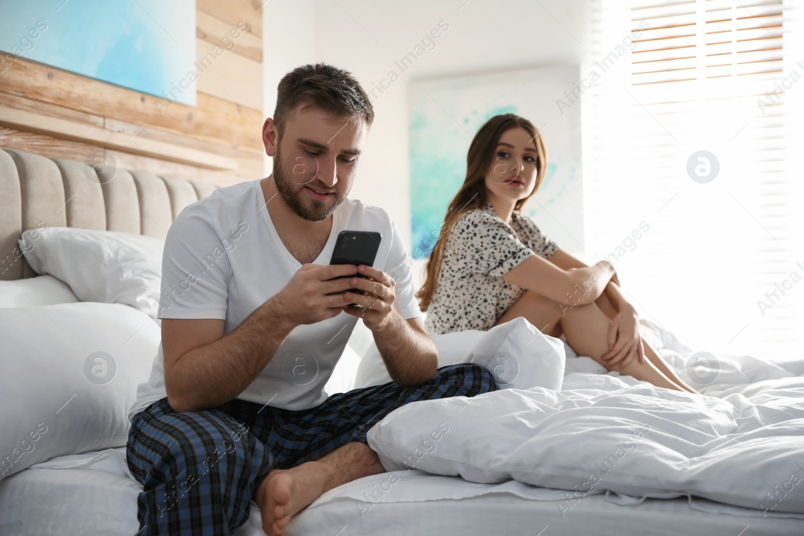 Photo of Distrustful young woman peering into boyfriend's smartphone at home. Jealousy in relationship