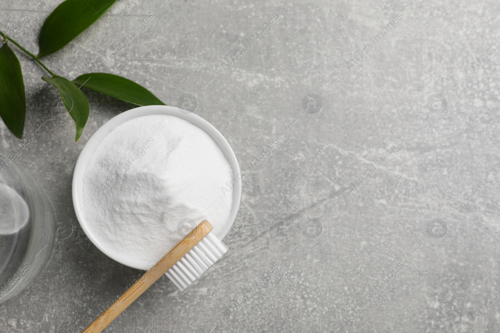 Photo of Bamboo toothbrush, green leaf and bowl of baking soda on grey table, flat lay. Space for text