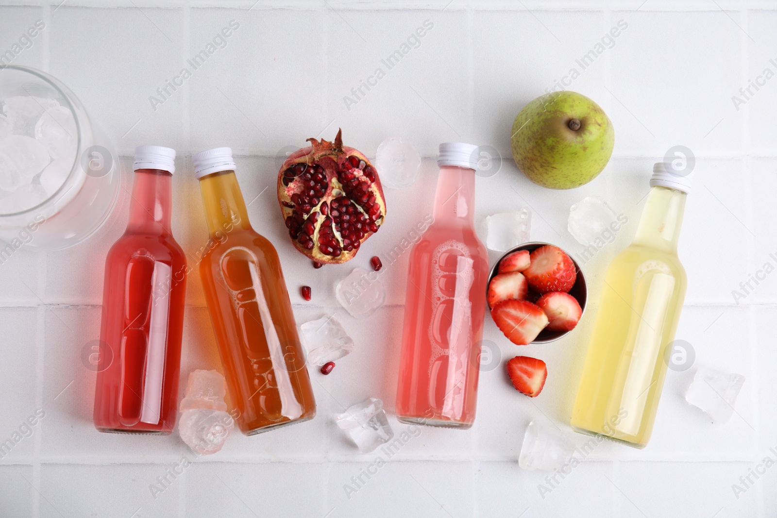 Photo of Tasty kombucha in glass bottles, fresh fruits and ice on white table, flat lay