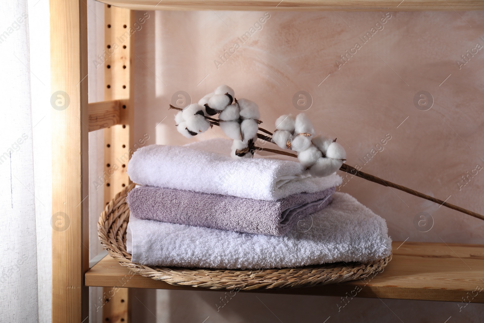 Photo of Stacked soft towels and cotton branch on wooden shelf indoors