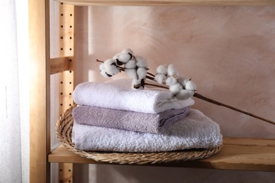 Stacked soft towels and cotton branch on wooden shelf indoors