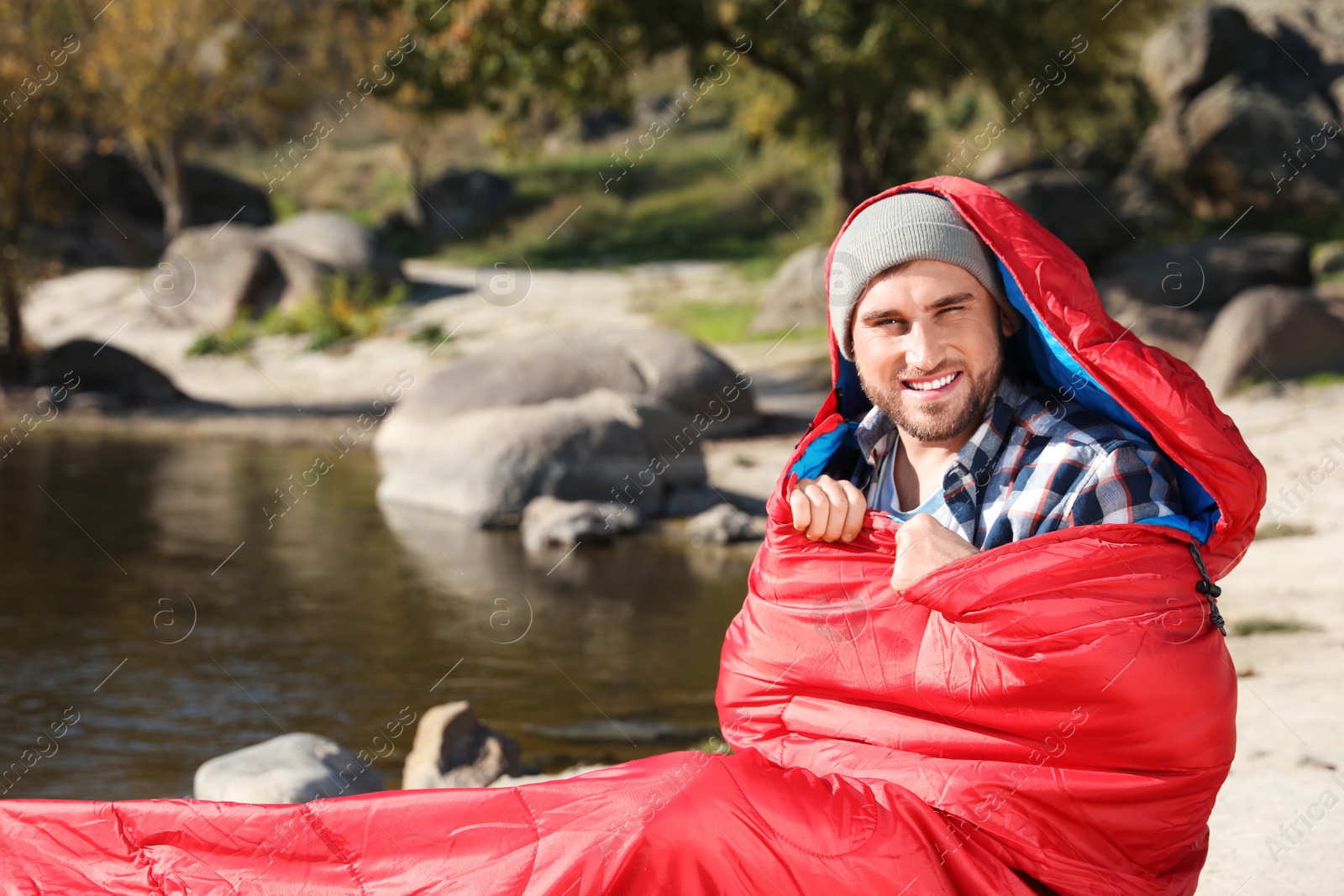 Photo of Male camper in sleeping bag near pond. Space for text