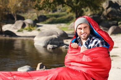 Male camper in sleeping bag near pond. Space for text