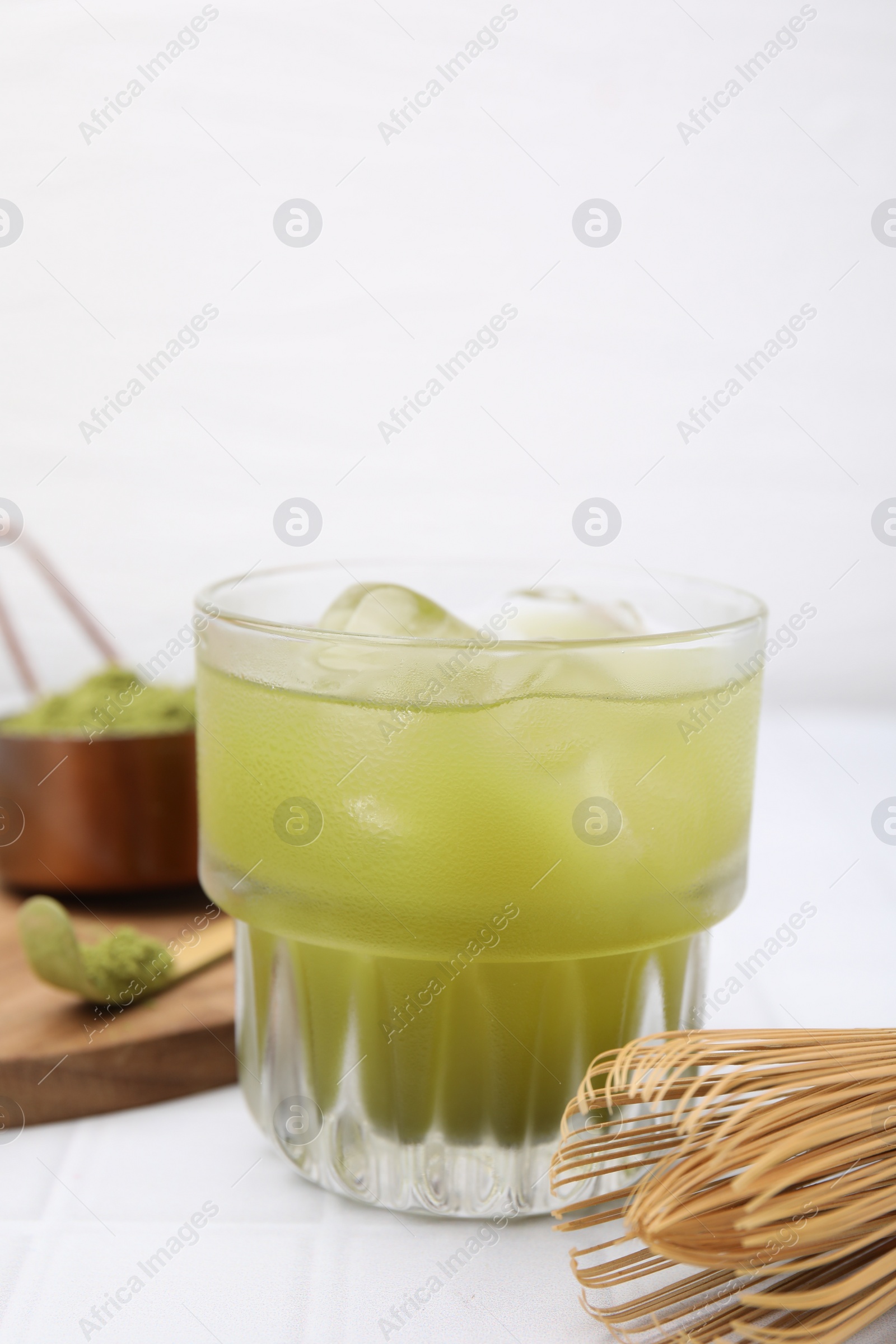 Photo of Glass of delicious iced green matcha tea and bamboo whisk on white tiled table, closeup. Space for text