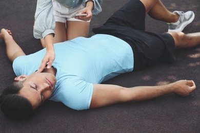 Photo of Young woman checking pulse of unconscious man outdoors. First aid