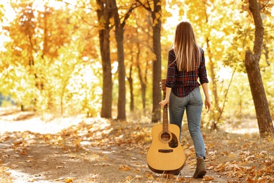 Photo of Teen girl with acoustic guitar in autumn park, back view
