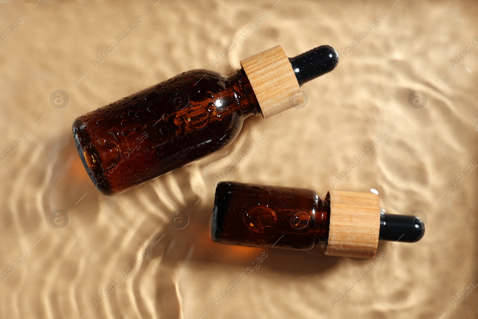 Photo of Bottles of cosmetic product in water on beige background, flat lay