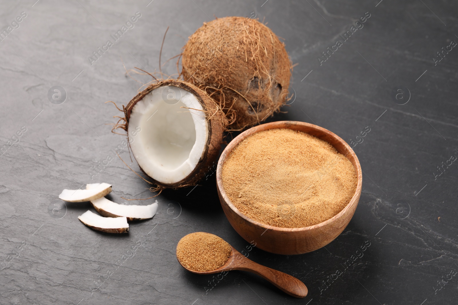 Photo of Spoon with coconut sugar, bowl and fruits on dark textured table, closeup