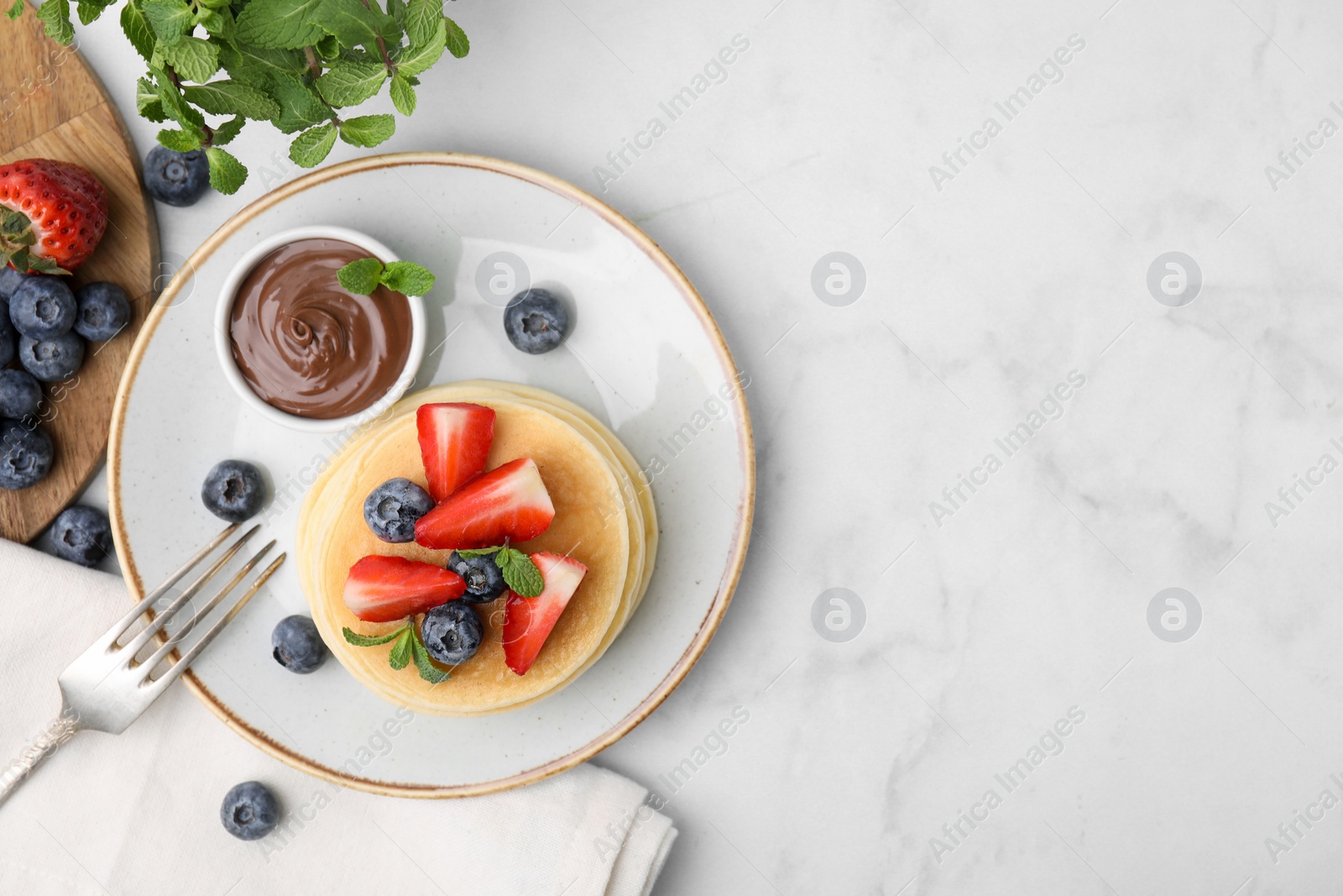 Photo of Delicious pancakes with strawberries, blueberries, mint and chocolate sauce served on light marble table, flat lay. Space for text