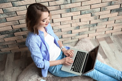 Photo of Beautiful young woman using laptop while sitting on floor near brick wall