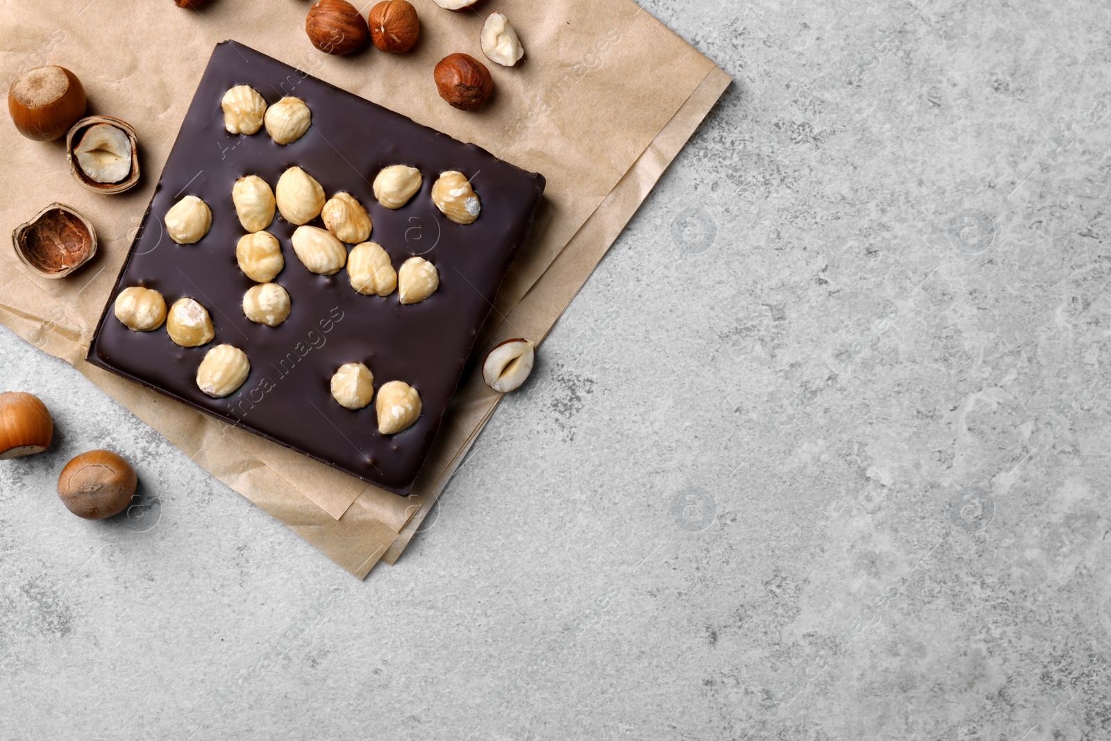 Photo of Delicious chocolate bar and hazelnuts on light grey table, flat lay. Space for text