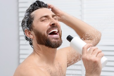 Photo of Happy man with bottle of shampoo singing in shower