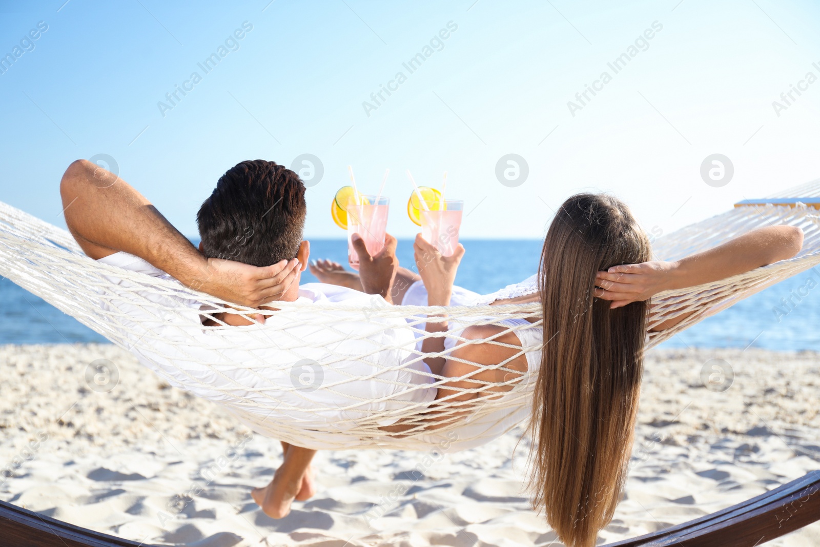 Photo of Couple with refreshing cocktails relaxing in hammock on beach