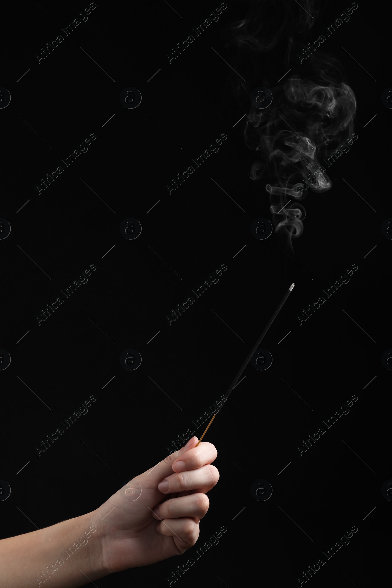 Photo of Woman holding smoldering incense stick on black background, closeup