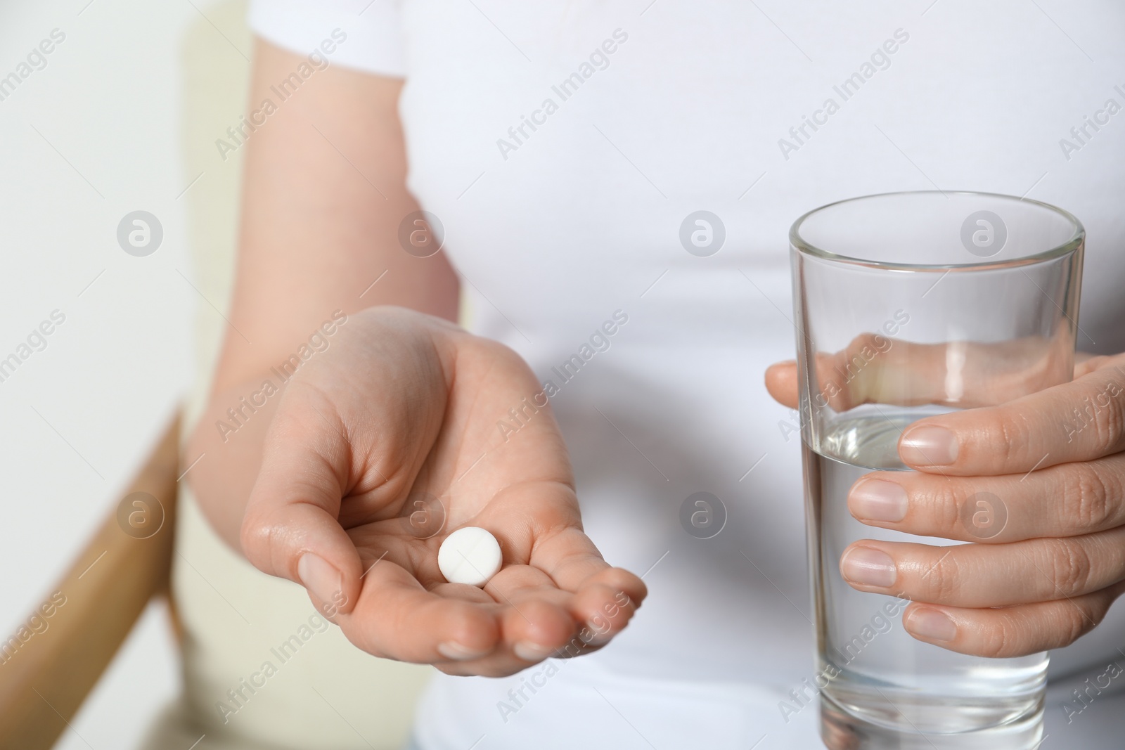 Photo of Woman with glass of water and pill on blurred background, closeup