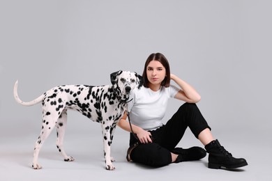 Beautiful young woman with her adorable Dalmatian dog on light grey background. Lovely pet