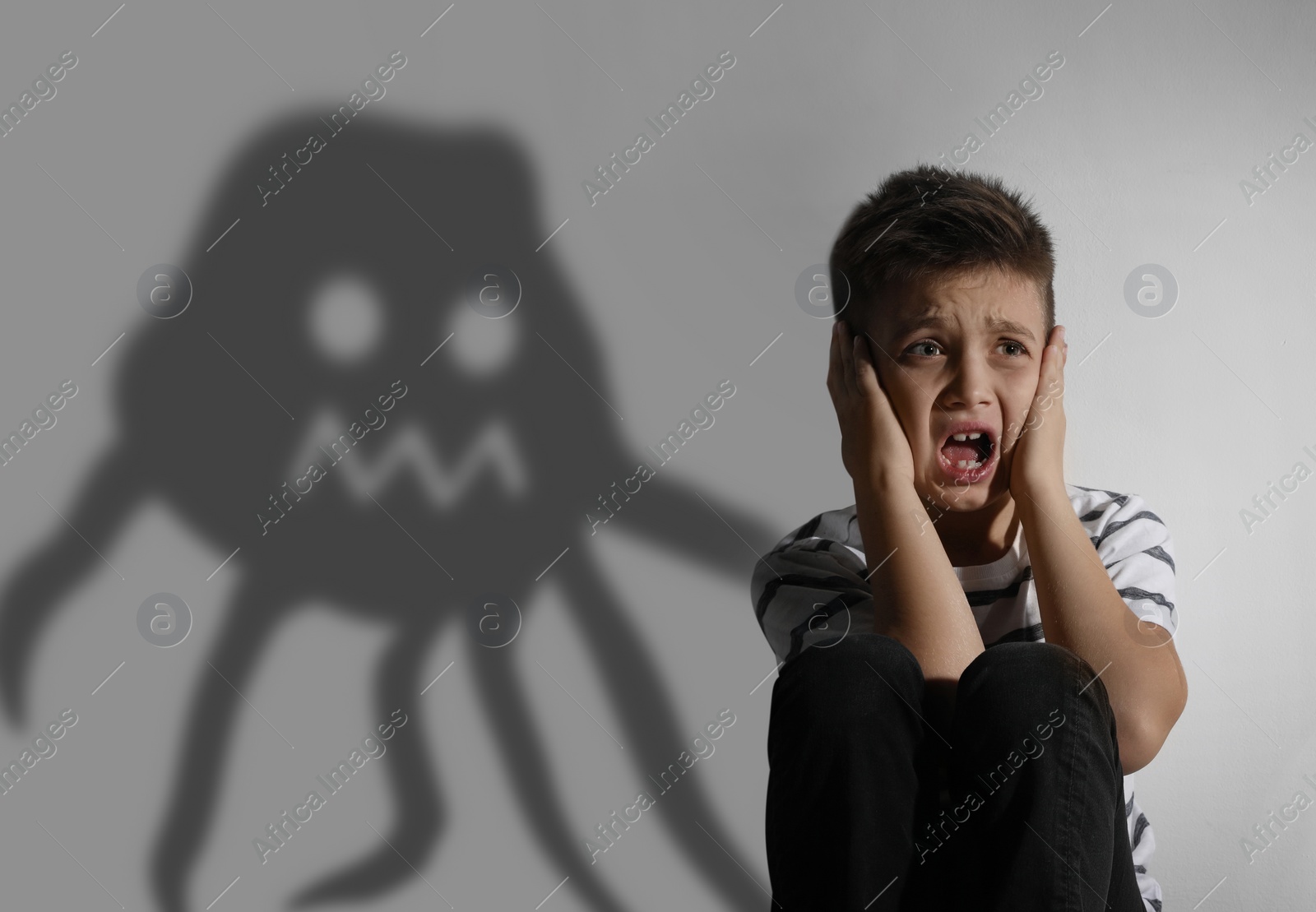 Image of Scared little boy suffering from sciophobia and phantom behind him. Irrational fear of shadows