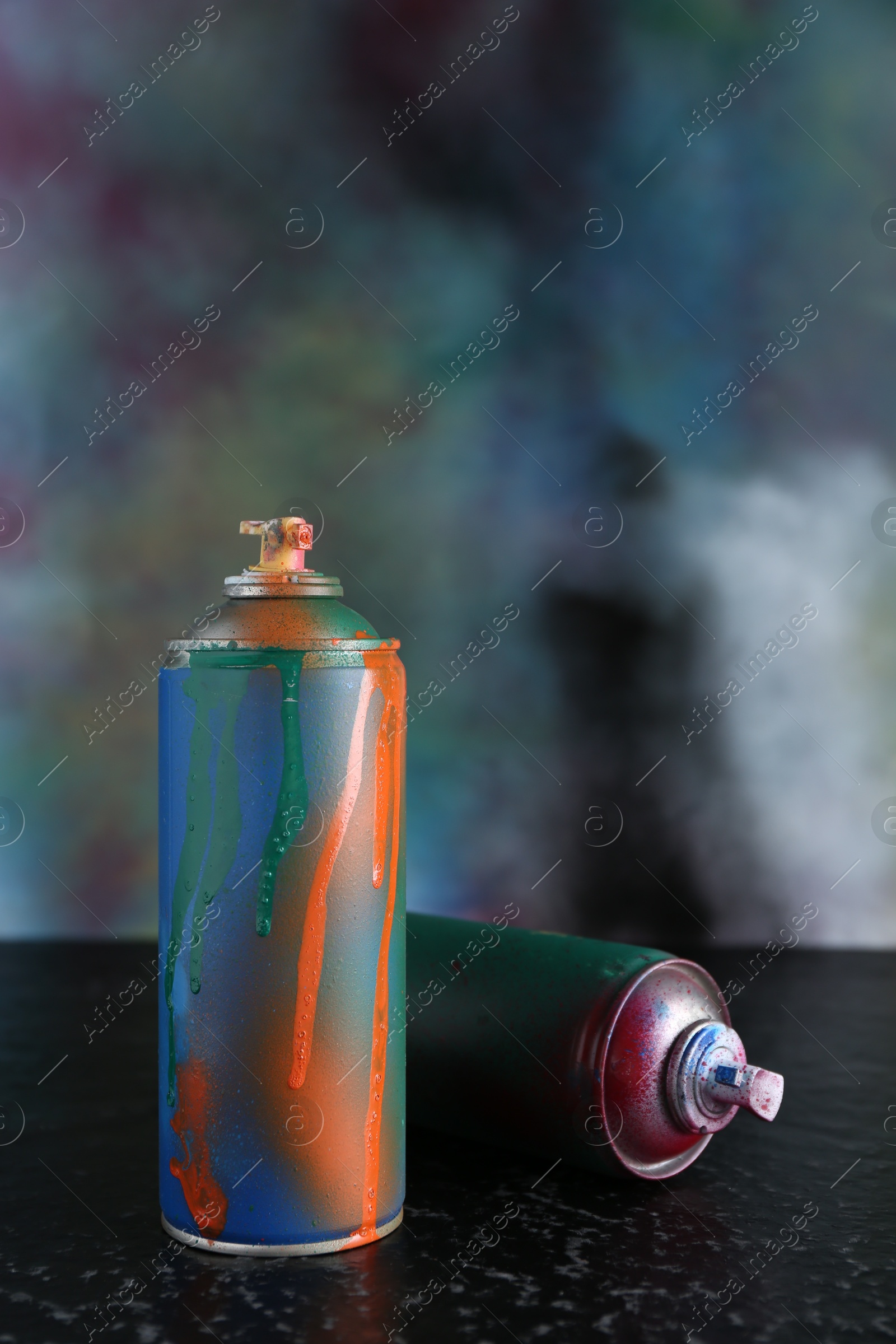 Photo of Two spray paint cans on black textured surface against color background