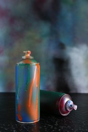 Photo of Two spray paint cans on black textured surface against color background