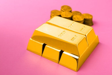 Shiny gold bars and coins on color background