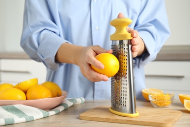 Woman zesting lemon at table indoors, closeup